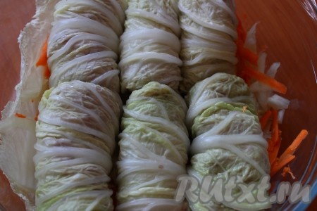 Одну морковку вымыть, очистить и натереть на крупной тёрке. На дно жаропрочной формы выложить несколько листьев капусты (которые мы откладывали в сторонку), посыпать натертой морковкой. На это овощное "одеяло" выложить подготовленные голубцы.
