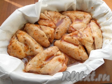 Форму для запекания застелить пергаментом, добавить растительное масло и выложить в нее куриные крылышки вместе с маринадом.
