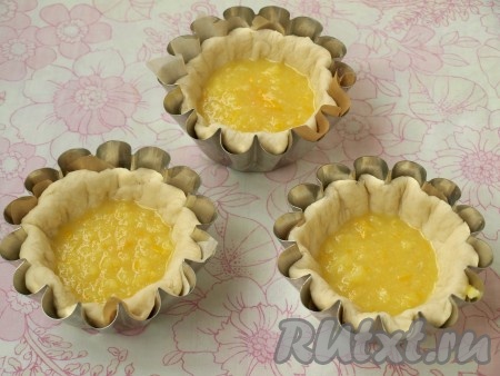 Затем от каждой части отщипнуть четверть для формирования верха. Из оставшегося теста сделать корзиночки. Если использовать металлические формы, как у меня, то их нужно застелить пекарской бумагой, вырезав её по размеру формочек. Раскатать лепёшку и вложить её в формочку, прижав к стенкам. Взбить венчиком яйцо и добавить его в&nbsp; лимонную начинку. Распределить начинку по всем булочкам, это, приблизительно, 2,5-3 столовых ложки.
