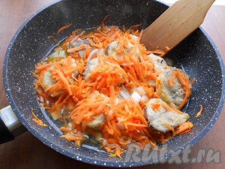 На сковороде разогреть растительное масло и обжарить хека на среднем огне с двух сторон до румяного цвета. Затем лук репчатый, нарезанный тонкими кусочками, и натёртую на крупной терке морковь добавить в сковороду, аккуратно распределить между кусочками рыбы.
