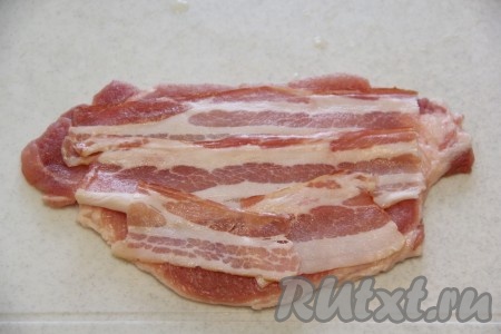Огурчики нарезать на длинные брусочки. На каждый отбитый кусок свинины выложить пару кусочков бекона в один слой.