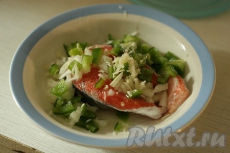 Стейк форели выкладываем в глубокую тарелку, сверху овощи, тертый чеснок и заливаем вином. 