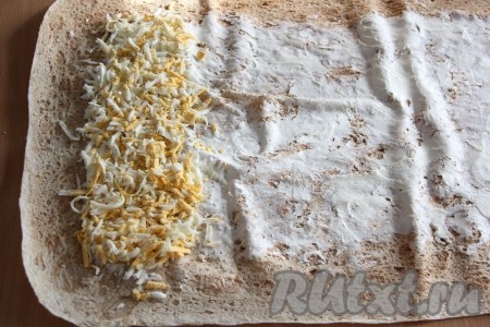 Все ингредиенты будем выкладывать поверх смазанной части лаваша. Яйца натереть на крупной тёрке, выложить вдоль короткой части лаваша в виде полоски.